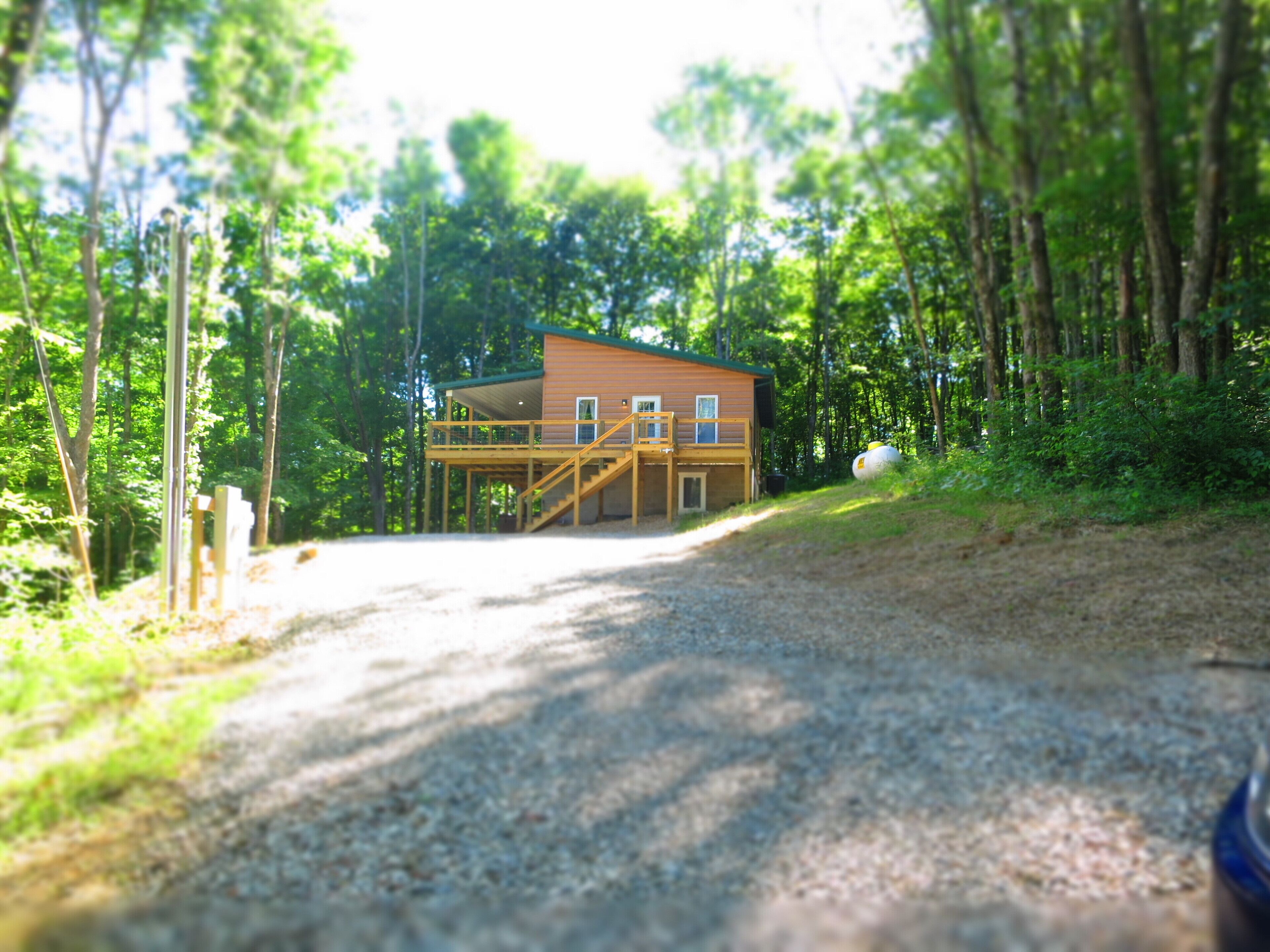 A cabin with a deck and a covered porch, surrounded by a forest.