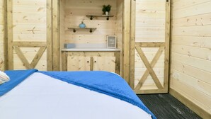 A room with a bed, wooden walls, a sliding barn door, a shelf with a vase and a sign, and a small plant. - Rocky Pine Cabin. Hot Tub, and Pet Friendly! (Nelsonville)