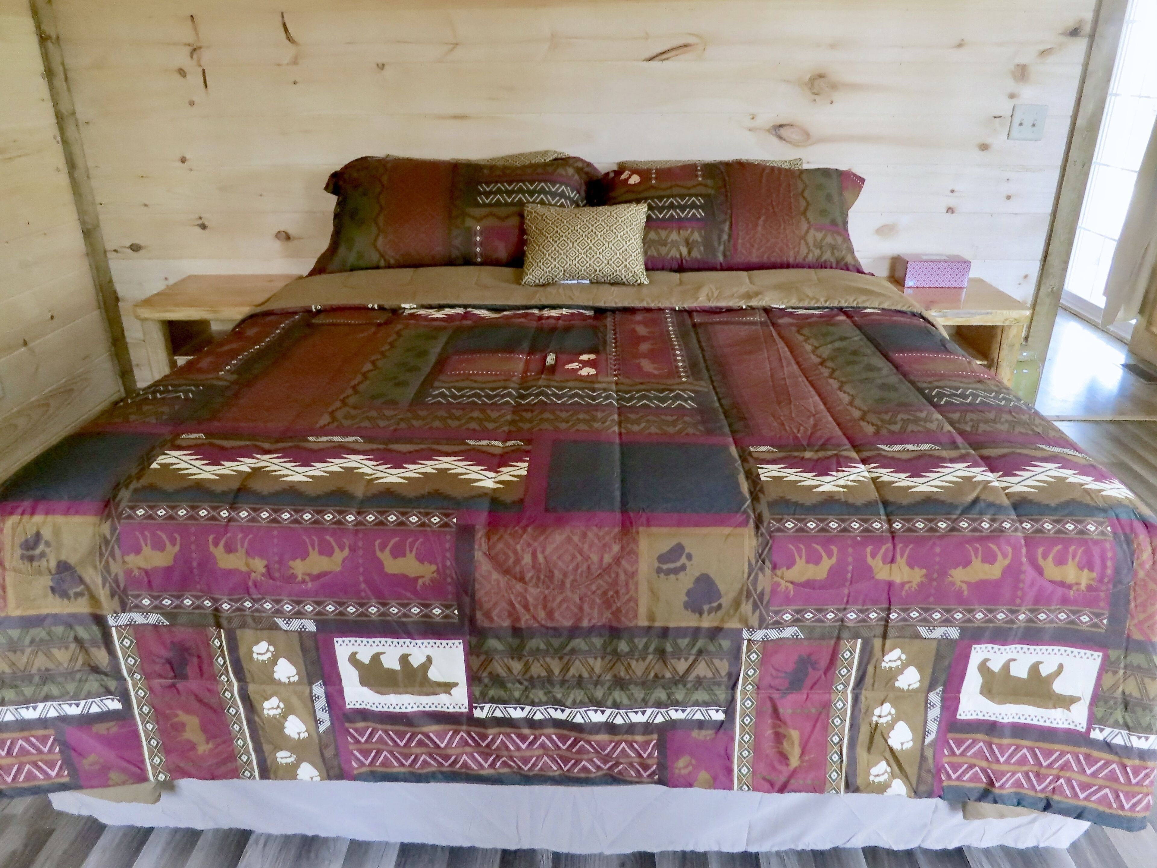 A wooden cabin bedroom with a bed covered in a patchwork quilt, a wooden nightstand, and a small table.