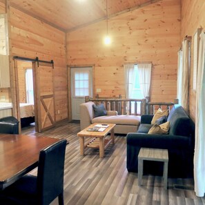 Interior de uma cabana de madeira com um sofá, uma mesa de jantar e uma pequena mesa com livros.