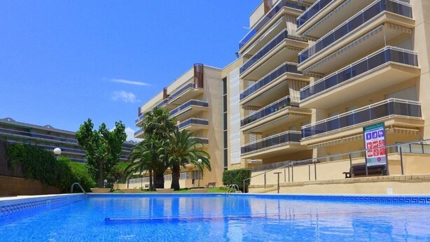 Una piscina con superficie de agua azul cristalina, rodeada por un edificio de varios pisos con balcones.