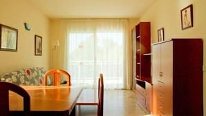 Una habitación con una mesa de comedor de madera, dos sillas, un sofá floral, un ventanal con cortinas translúcidas y un armario de madera.