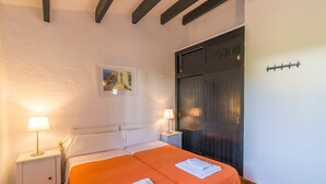 Ein Doppelbett mit orangefarbener Bettdecke, ein Nachttisch mit Lampe, ein Gemälde an der Wand und eine dunkle Tür.