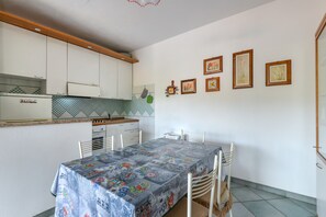 Une cuisine compacte avec des meubles blancs, une table à manger recouverte d’une nappe à motifs et un petit réfrigérateur.