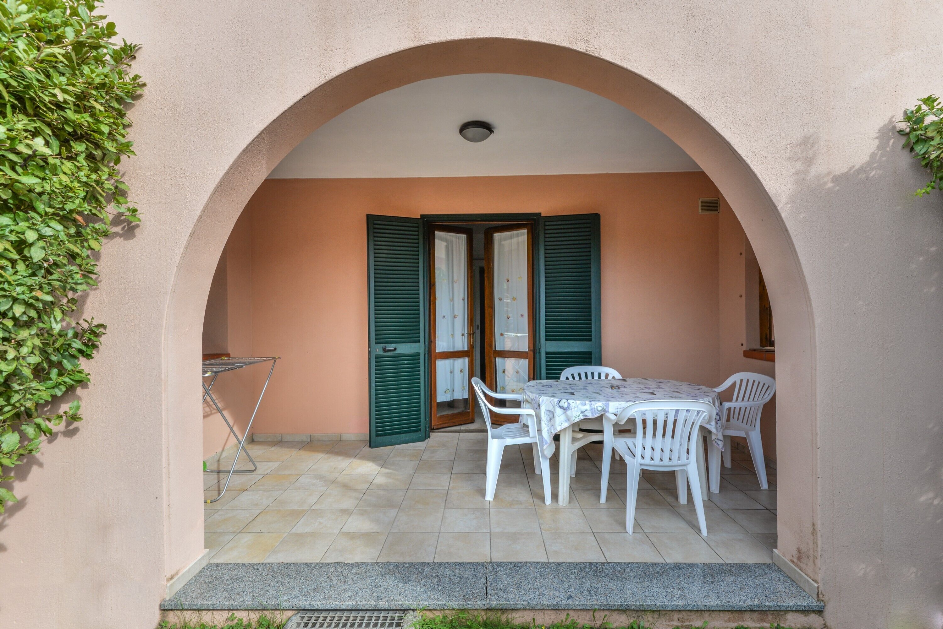 An outdoor patio with a table and chairs, an archway, and a door with shutters.