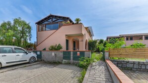 A modern building with a car parked in front, a paved driveway, and a stone wall. - Apartment '3B' with Private Terrace and Air Conditioning (Campo nell'Elba)