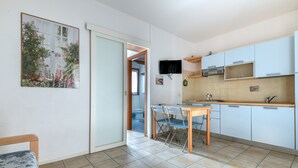 A kitchen with a dining table and chairs, a TV mounted above the counter, and a door leading to another room. - Apartment '3B' with Private Terrace and Air Conditioning (Campo nell'Elba)