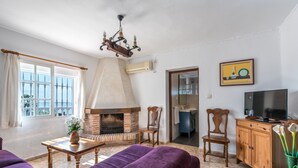 Een woonkamer met een open haard, een televisie en uitzicht op de natuur.