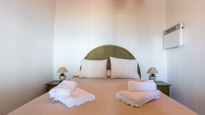 Een opgemaakt bed met twee kussens, twee handdoeken gevouwen en een wandairconditioner.