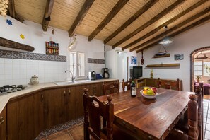 A kitchen with wooden cabinets, a tiled backsplash, a wooden dining table, and a hanging light fixture.