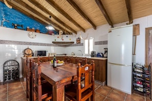 A kitchen with a wooden dining table, chairs, a refrigerator, and a wine rack.