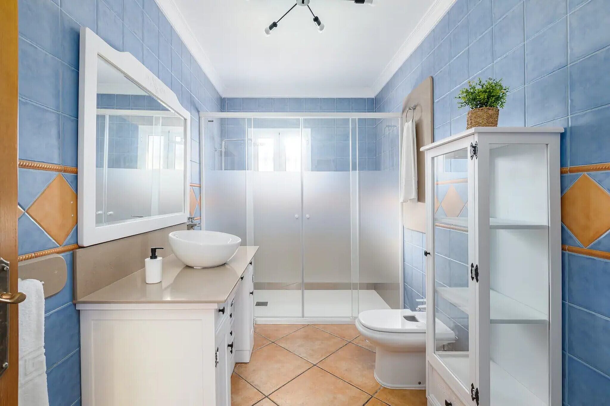 Een badkamer met een wit wastafel, een toilet, een douche met glazen wanden en een kast met planken.
