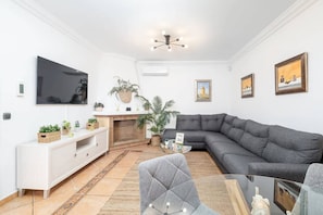 A living room with a grey sectional sofa, a flat-screen TV, a white console table, a fireplace, and a ceiling light fixture. - Country House Zambrana with Heated Pool (Cartama)