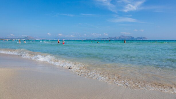 A beach with clear water, a sandy shore, and distant mountains.