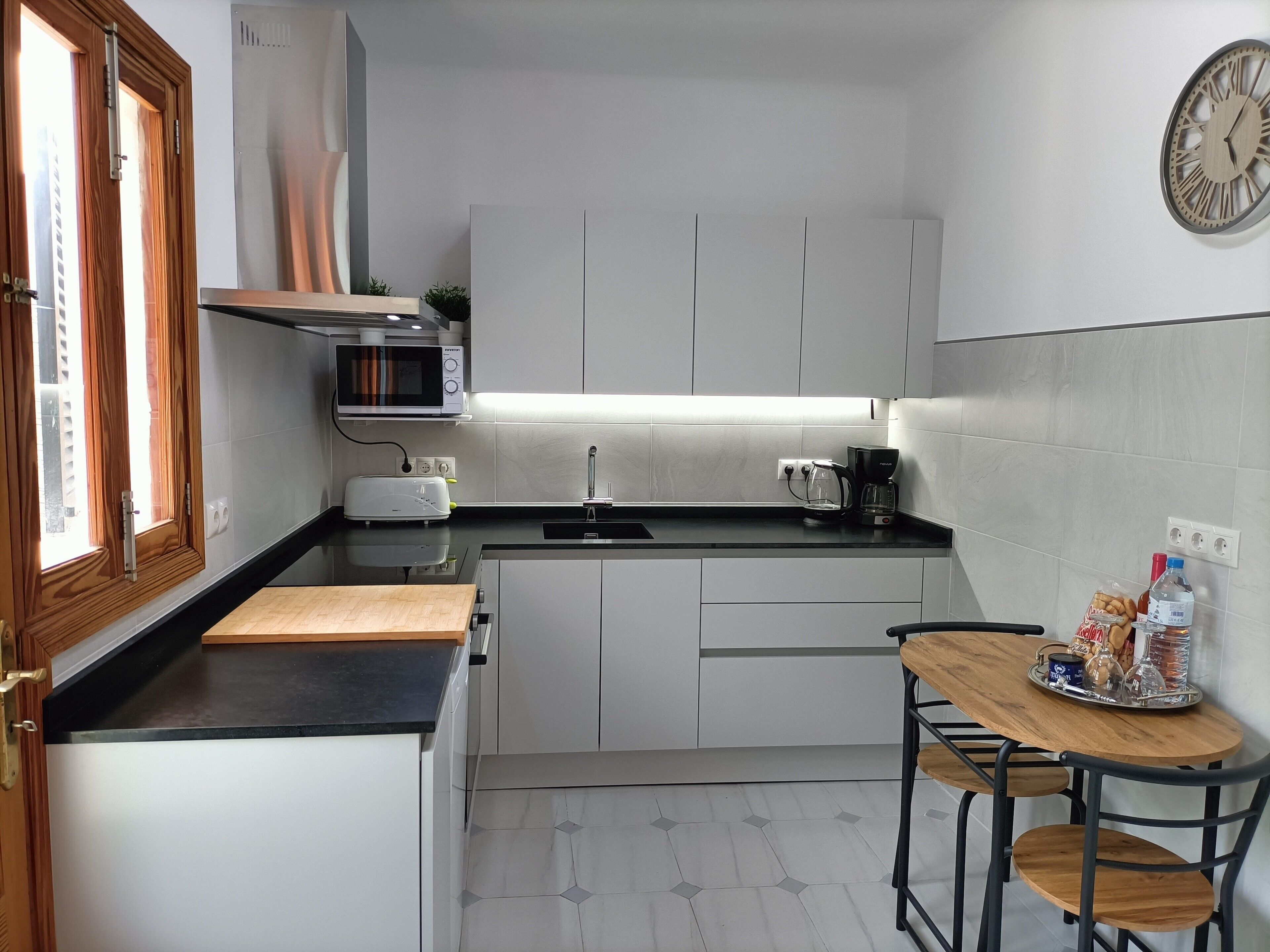 Une cuisine compacte avec des meubles blancs, un four à micro-ondes, un grille-pain, une machine à café et une petite table à manger avec des chaises.
