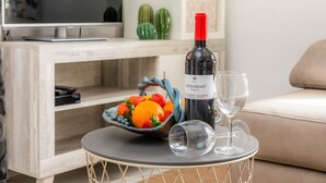 A modern living room with a television, a wine bottle, a bowl of fruit, and a glass on a round table.
