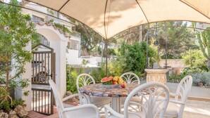 An outdoor patio with a round table, white wicker chairs, and a fruit bowl.