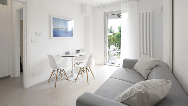 Una sala moderna con un sofá gris, una mesa de comedor redonda con sillas, un cuadro en la pared y un ventanal corredero que da a un área exterior.