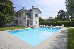 A two-story house with a swimming pool, a balcony, and a well-maintained lawn.