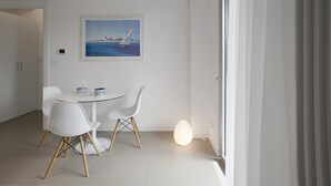 Un comedor moderno con una mesa redonda, sillas blancas, un cuadro de un velero y una lámpara de pie encendida.