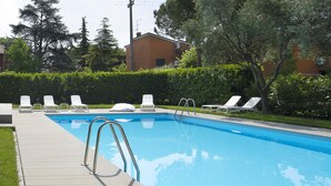 Una piscina con escalera metálica, rodeada de sillas de descanso blancas y un seto.