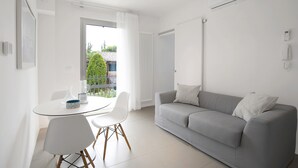Una sala moderna con un sofá gris, una mesa redonda de cristal y sillas blancas.