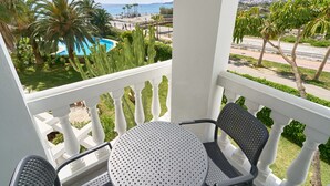 A balcony with a table and chairs, overlooking a pool and palm trees. - Bright Apartment Estela Maris with Direct Beach Access (Nerja)