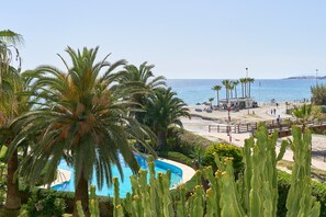 Una piscina rodeada de palmeras y cactus, con vista a la playa y al océano.