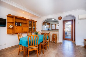 A dining area with a table set for six, wooden chairs, a blue tablecloth, and a wooden cabinet with glass doors. - Centrally located with a rooftop terrace – Casa Sa Torre III (Canyamel)
