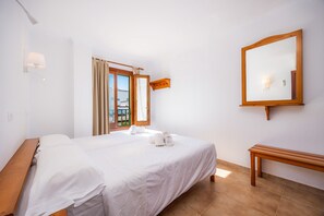 A hotel room with a bed, a wooden bench, a wall-mounted mirror, and a window with curtains. - Centrally located with a rooftop terrace – Casa Sa Torre III (Canyamel)