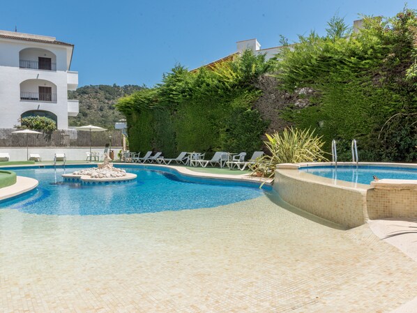 Une piscine avec des chaises longues et une petite fontaine.