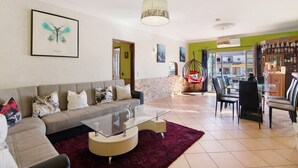 A living room with a sofa, coffee table, and chairs, a dining area with a table and chairs, and a kitchen visible through an open doorway. - Mediterranean Villa "Calipso" with Wi-Fi, Terrace and Pool (Albufeira)