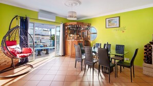 A dining area with a glass table and chairs, a hanging chair, and a bar area with bottles. - Mediterranean Villa "Calipso" with Wi-Fi, Terrace and Pool (Albufeira)