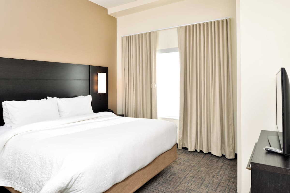 Ein Hotelzimmer mit einem großen Bett, einem Flachbildfernseher und einem Vorhangfenster.