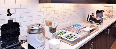 A breakfast bar with waffle makers, a coffee station, and various food items.