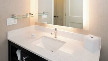A bathroom with a white sink, a glass shelf, a mirror, and a door in the background.