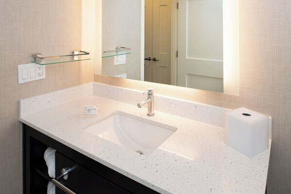 Un baño con un lavabo blanco, un estante de cristal, un espejo y una puerta al fondo.
