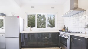 Een moderne keuken met een roestvrijstalen koelkast, zwarte kastjes, een gasfornuis en een raam met uitzicht op bomen.