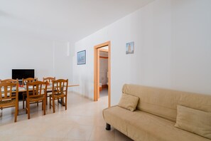 A dining area with a table and chairs, a sofa, and a doorway leading to another room.