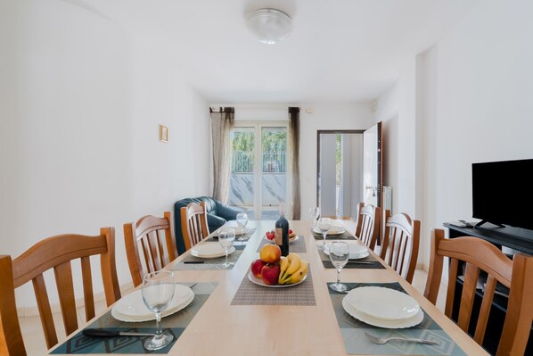 A dining area with a long table, chairs, a fruit bowl, and a television.