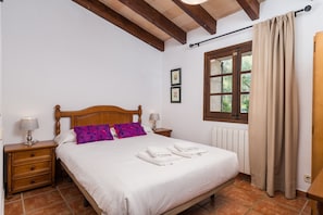 A bedroom with a wooden bed, two bedside tables with lamps, a window with curtains, and a radiator.
