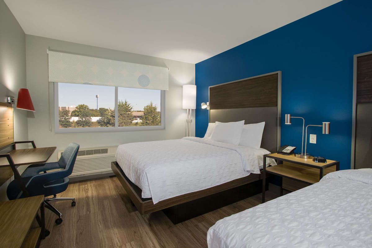 Une chambre d’hôtel avec un grand lit, un bureau, une chaise et une fenêtre donnant sur des arbres et des immeubles.