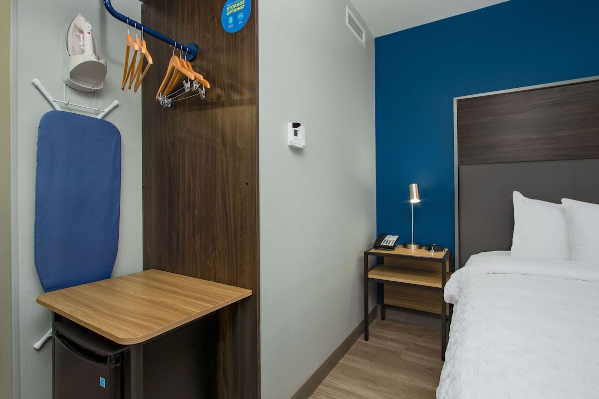 Une chambre d’hôtel équipée d’un lit, d’un bureau, d’une chaise, d’une planche à repasser et d’une armoire.