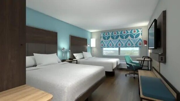Habitación de hotel con dos camas, un escritorio, una silla y un televisor.