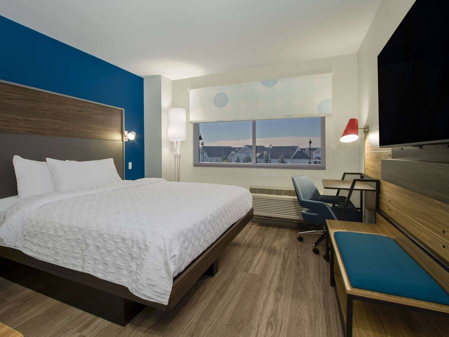 A hotel room with a large bed, a desk, a chair, a TV, and a window with a city view.