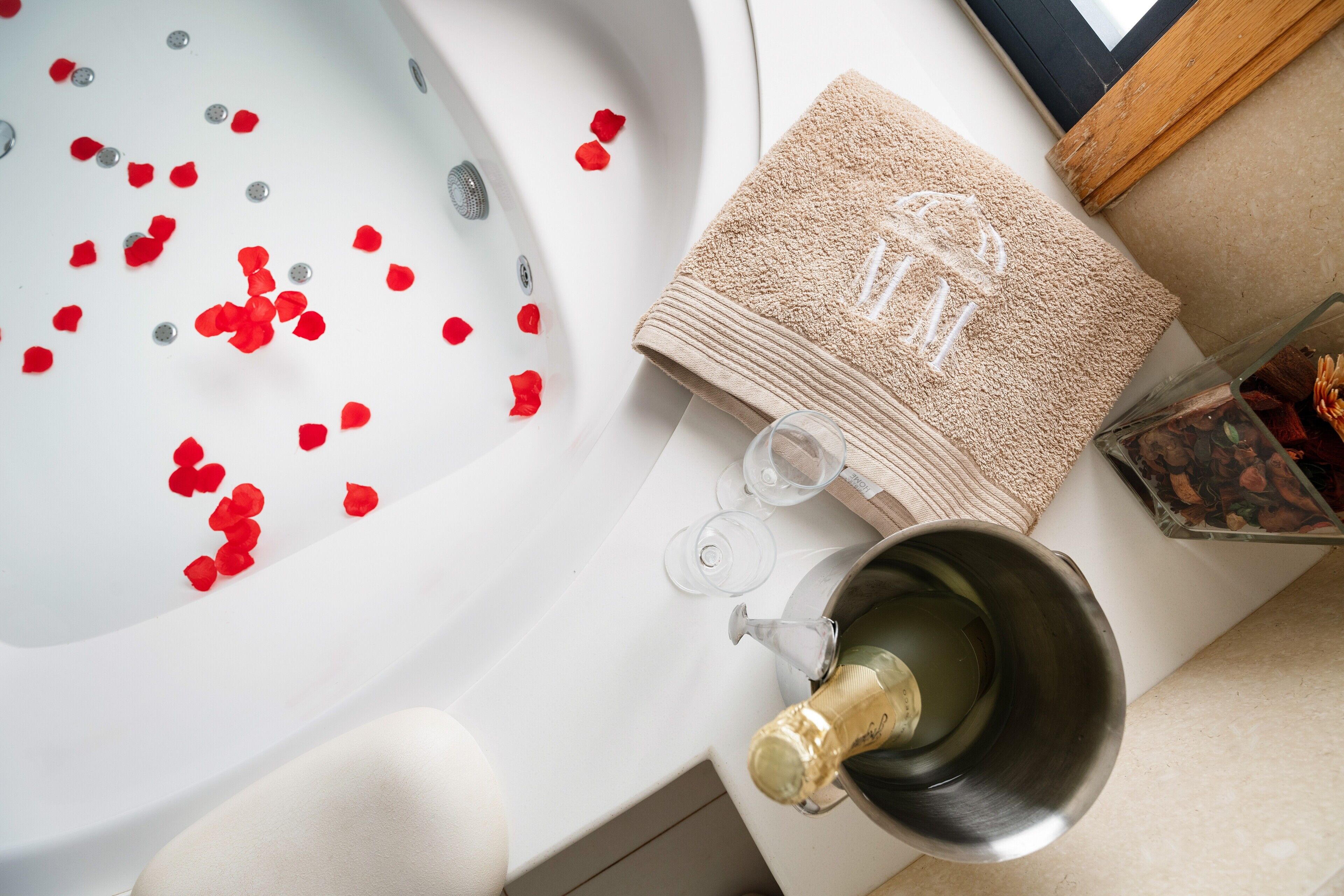 A bathtub with red rose petals, a towel, and a champagne bottle.