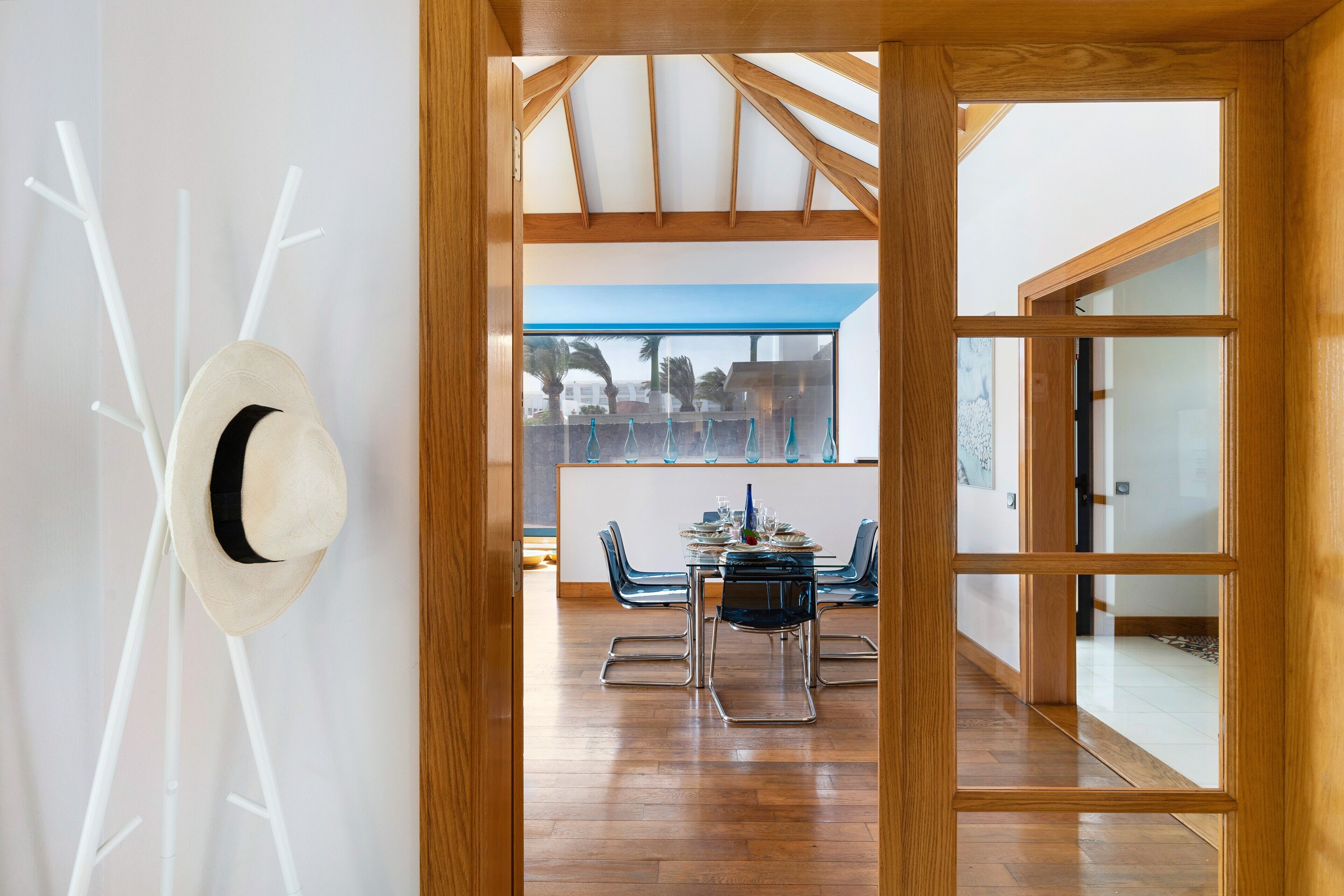A modern interior with a dining area, wooden ceiling, and a view through a glass door.