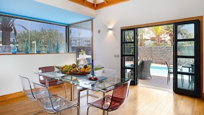 Un espace repas moderne avec une table en verre, des chaises transparentes et une vue sur une piscine.