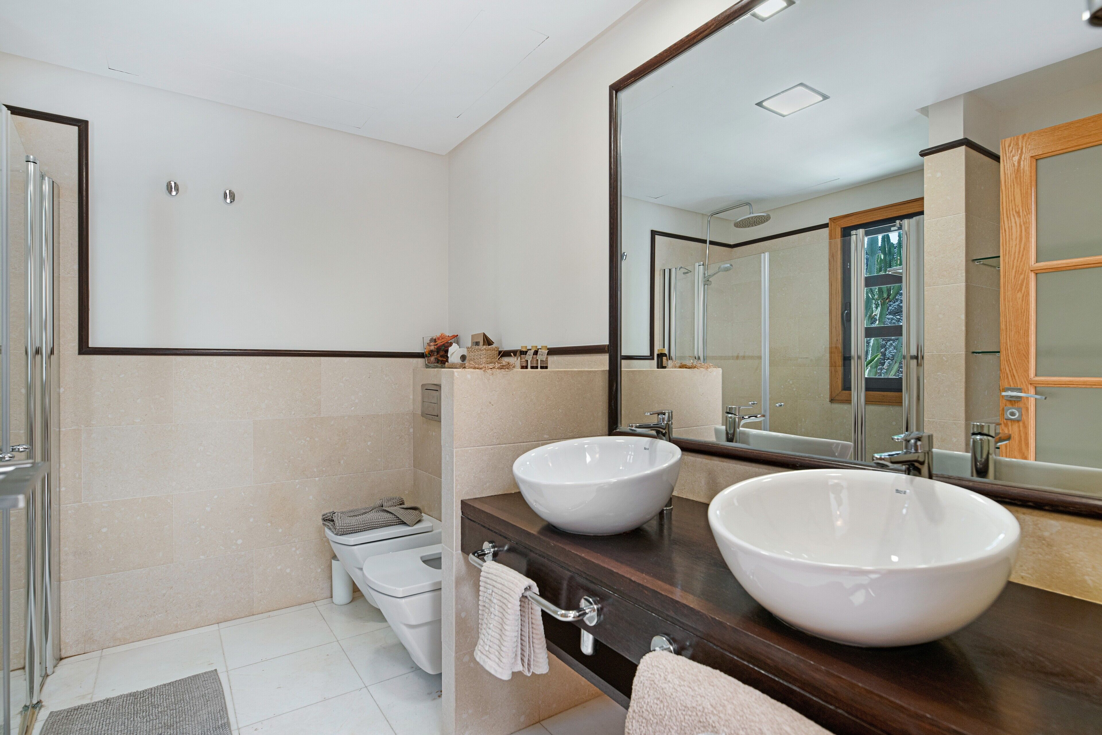 A modern bathroom with two large white sinks, a glass shower enclosure, and a large mirror.