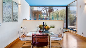 Un espace repas avec une table en verre, des chaises transparentes et une vue dégagée sur l’extérieur grâce à une grande fenêtre.